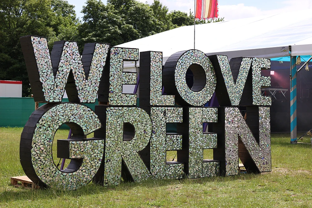 Large decorative letters at an outdoor festival spelling “We Love Green” for sustainability. (source : luniwave.com)